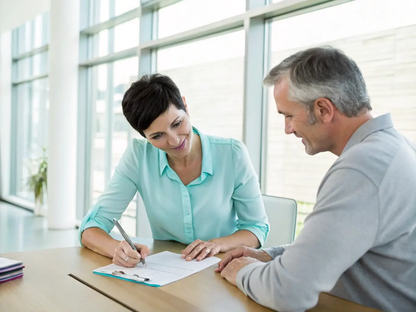 A friendly insurance broker sitting at a desk, smiling and discussing insurance options with a client in a bright, modern office setting, emphasizing a personal and trusting relationship.